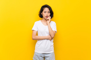 Asian young woman over isolated yellow wall surprised and shocked while looking right