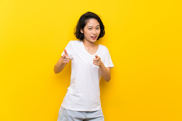 Asian young woman over isolated yellow wall pointing to the front and smiling
