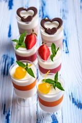 Mousse desserts in wineglasses, decorated chocolate, strawberry, mint and cocktail cherries on aged wooden table.