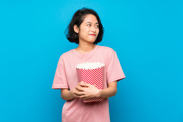 Asian young woman eating popcorns making doubts gesture while lifting the shoulders