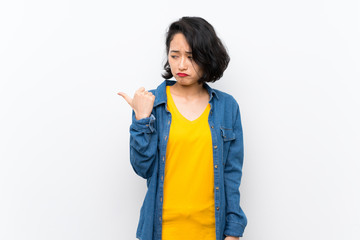 Asian young woman over isolated white background unhappy and pointing to the side