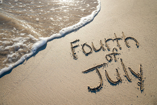 Fourth of July message written for the American Independence Day holiday in smooth sand with incoming wave on the beach
