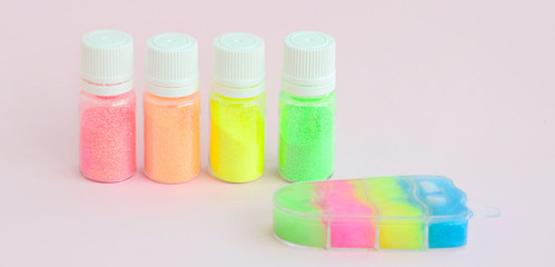 Colorful glitters lies on pastel pink background. Many round jars with multi-colored bright sparkles for nail polish
