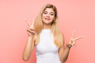 Teenager girl over isolated pink background smiling and showing victory sign