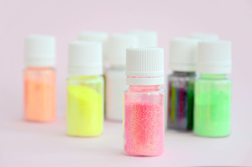 Colorful glitters lies on pastel pink background. Many round jars with multi-colored bright sparkles for nail polish