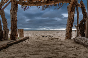 Shipwrecked on a desert island.  Looking out at an approaching storm from a homemade shelter made...