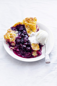 A piece of a cherry pie with a lattice and flaky crust shot on a white fabric served with vanilla ice cream