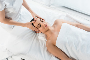 Fototapeta na wymiar overhead view of masseur doing head massage to pretty woman on massage table