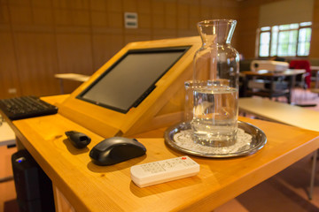 Blurred wooden trubune in a conference or lecture hall with a water pitcher and a computer