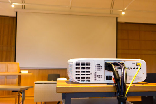 White screen projector in front of a screen in a conference or seminar hall with a white projector screen