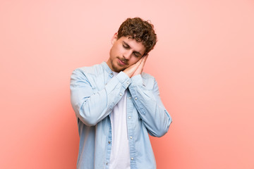 Blonde man over pink wall making sleep gesture in dorable expression