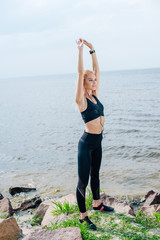 happy athletic girl stretching and listening music near sea