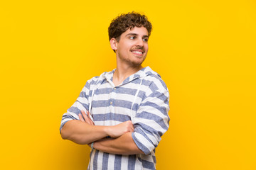 Blonde man over yellow wall with arms crossed