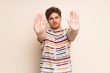Fototapeta premium Blonde man over isolated wall making stop gesture and disappointed