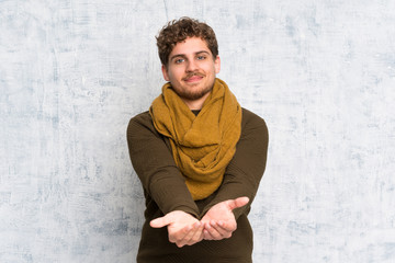 Blonde man over grunge wall holding copyspace imaginary on the palm to insert an ad