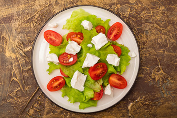 plate of salad with cherry tomatoes, soft brynza cheese and lettuce leaves. dressing with olive oil. Dietary dish. Top view