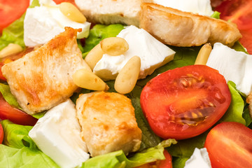 salad with warm chicken, cherry tomatoes and soft brynza cheese, decorated with pine nuts. dressing with olive oil. dressing with olive oil. Close up