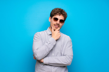 Obraz premium Blonde man over blue wall with glasses and smiling
