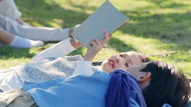 beautiful little asian girl and boy sister and brother lying on grass reading a book together in park