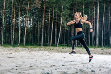 attractive and sportive blonde woman running near green trees