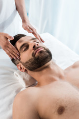 cropped view of young woman doing massage to handsome man with closed eyes