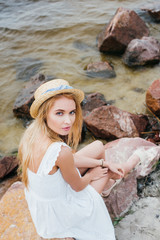 overhead view of beautiful woman in straw hat sitting on stones and looking at camera