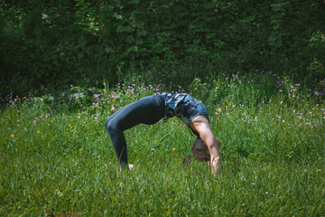 Fototapeta na wymiar Blonde girl doing bridge yoga pose in the nature. Yoga concept
