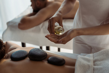 cropped view of masseur holding bottle with oil near woman and man in spa center