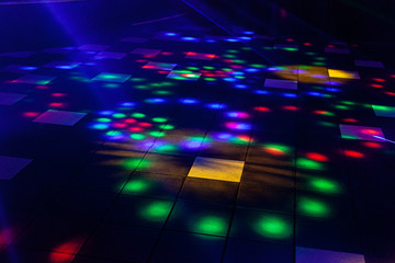 Bright nightclub red, green, purple, white, pink, blue laser lights cutting through smoke machine smoke making light and rainbow patterns on the dance floor with bokeh in the background. Mardi Gras