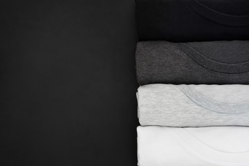 top view stack of black, grey and white (monochrome) t-shirt rolled up on black background, copy...