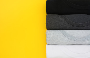 top view stack of black, grey and white (monochrome) t-shirt rolled up on yellow background, copy space, flat lay
