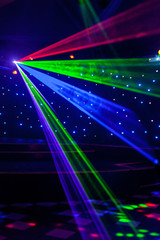Bright nightclub red, green, purple, white, pink, blue laser lights cutting through smoke machine smoke making light and rainbow patterns on the dance floor with bokeh in the background. Mardi Gras