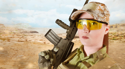 Portrait of young and beautiful military soldier woman holding an automatic rifle M16 on desert background with space for text.