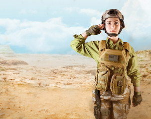 Young beautiful fully equipped military soldier woman in protective armor tactical vest, helmet, camouflage pants,holster and gloves standing and saluting on desert background with space for text.
