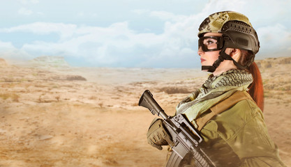 Side view portrait of young fully equipped military soldier woman holding an automatic rifle M16 on desert background with space for text.