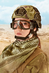 Portrait of fully equipped young military soldier woman in helmet, glasses and scarf on desert background.