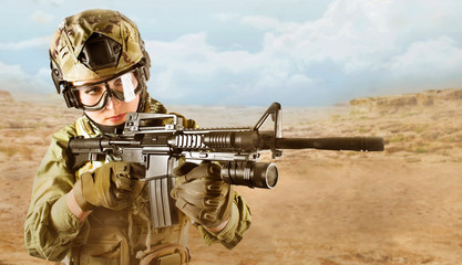 Beautiful fully equipped military soldier woman aiming at the enemy with automatic rifle M16 on desert background.
