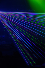Bright nightclub red, green, purple, white, pink, blue laser lights cutting through smoke machine smoke making light patterns on the dance floor with bokeh in the background. Mardi Gras inspiration