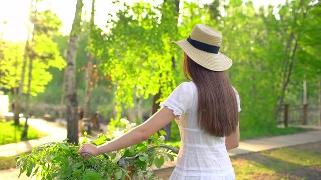 Young romantic beautiful traveler woman girl with hat and white dress with retro vintage bicycle in sunset forest. Riding on bike with basket of flowers. spring summer time nature park. Happy holiday