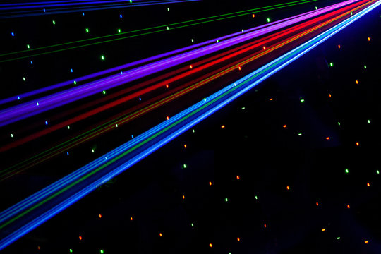 Bright nightclub red, green, purple, white, pink, blue laser lights cutting through smoke machine smoke making light patterns on the dance floor with bokeh in the background. Mardi Gras inspiration