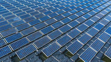 Solar panels in aerial view, rows array of polycrystalline silicon solar cells or photovoltaics in solar power plant floating on the water in lake.
