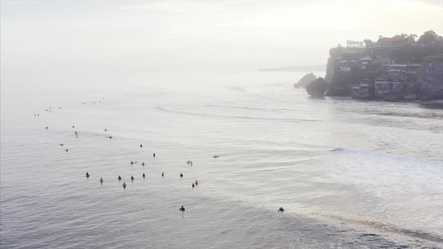 Static aerial view of famous Uluwatu spot and surfers waving on Indian ocean waves. On the background is cliff with houses, cfes, resorts, etc. Bali, Indonesia