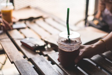 selective focus chocolate smoothie hold by woman hand on wooden table