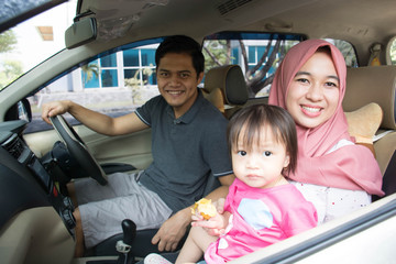 young muslim family , transport, leisure, road trip and people concept - happy man, woman and little girl traveling in a car looking out windows