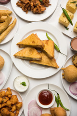 Indian Tea time snacks  in group includes Veg Samosa, Kachori/kachaudi, aloo bonda, khaman dhokla, bread, onion,chilli and moong pakora/pakoda/bhaji/bhajji/Bhajiya/bajji with sauces, selective focus