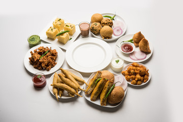 Indian Tea time snacks  in group includes Veg Samosa, Kachori/kachaudi, aloo bonda, khaman dhokla, bread, onion,chilli and moong pakora/pakoda/bhaji/bhajji/Bhajiya/bajji with sauces, selective focus