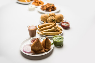 Indian Tea time snacks  in group includes Veg Samosa, Kachori/kachaudi, aloo bonda, khaman dhokla, bread, onion,chilli and moong pakora/pakoda/bhaji/bhajji/Bhajiya/bajji with sauces, selective focus