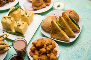 Indian Tea time snacks  in group includes Veg Samosa, Kachori/kachaudi, aloo bonda, khaman dhokla, bread, onion,chilli and moong pakora/pakoda/bhaji/bhajji/Bhajiya/bajji with sauces, selective focus