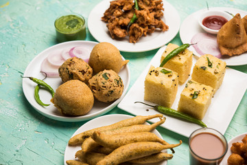 Indian Tea time snacks  in group includes Veg Samosa, Kachori/kachaudi, aloo bonda, khaman dhokla, bread, onion,chilli and moong pakora/pakoda/bhaji/bhajji/Bhajiya/bajji with sauces, selective focus