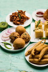Indian Tea time snacks  in group includes Veg Samosa, Kachori/kachaudi, aloo bonda, khaman dhokla, bread, onion,chilli and moong pakora/pakoda/bhaji/bhajji/Bhajiya/bajji with sauces, selective focus